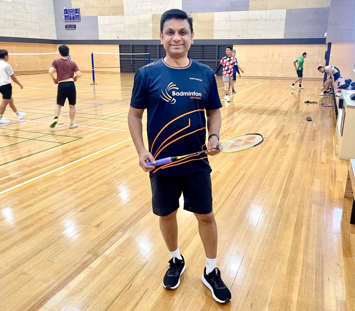 Coach Kiran holding a racket on the badminton court